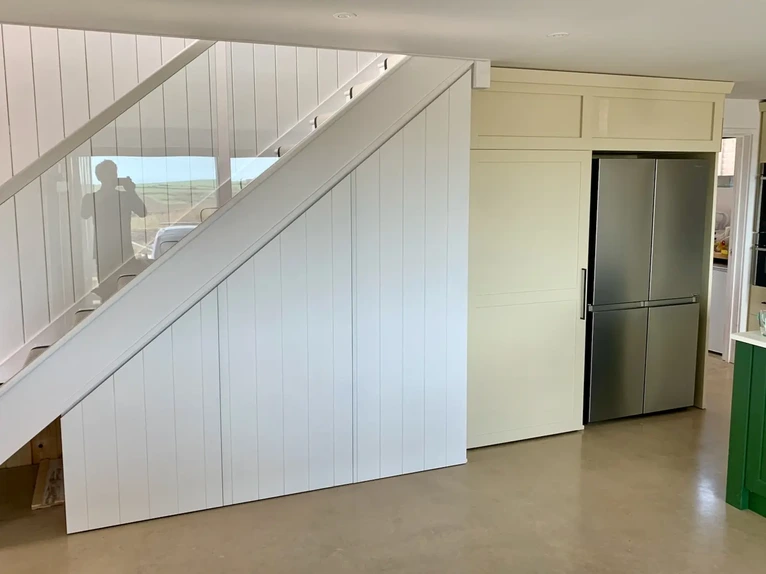 Custom built-in understairs storage unit featuring integrated cupboards, a desk nook, and fridge surround cabinetry